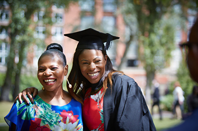 A graduate dressed in gown and mortarboard smiling with relative
