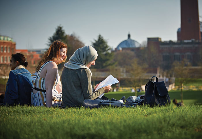 Students sitting on the grass overlooking Aston Webb Building