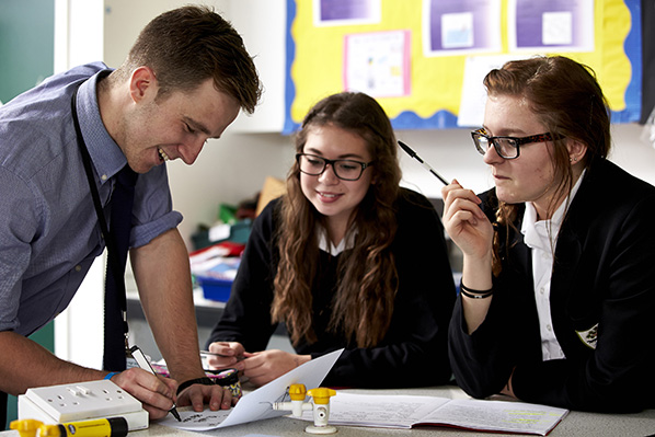Male teacher assisting two secondary school pupils with their work