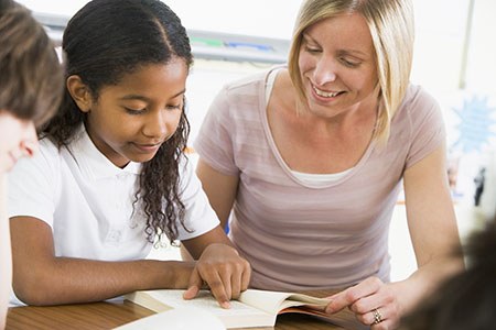 A teacher assiting a young girl with her reading in the classroom