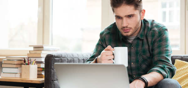 young man in green shirt sitting on sofa with laptop and mug