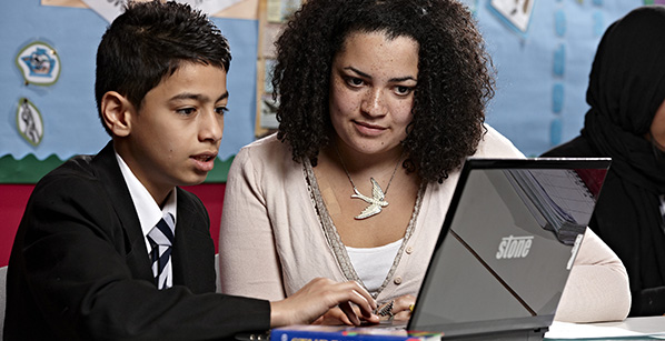 Female teacher assisting secondary school pupil with his classwork on a laptop