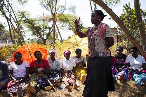 Kigali, Rwanda - August 27, 2013: Woman speaking to women sitting on the ground with her finger in the air.