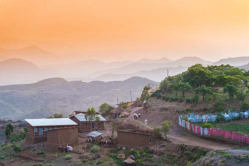 Rural village with one person walking in distance next to a red and blue fence between houses at sunset Lalibela Ethiopia Horn of Africa.
