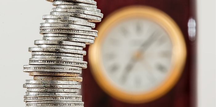 A stack of coins sat in front of a clock