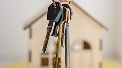 Keys held in front of a small model of a house