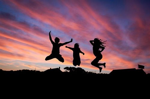 Three young people jumping into the air, silhouetted against an dusky sky