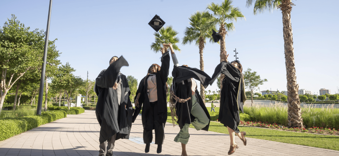 Graduates throwing caps outside in front of palm trees