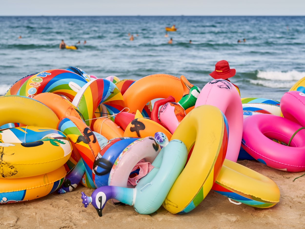 A pile of colourful inflatable rings on a beach with the sea in the distance