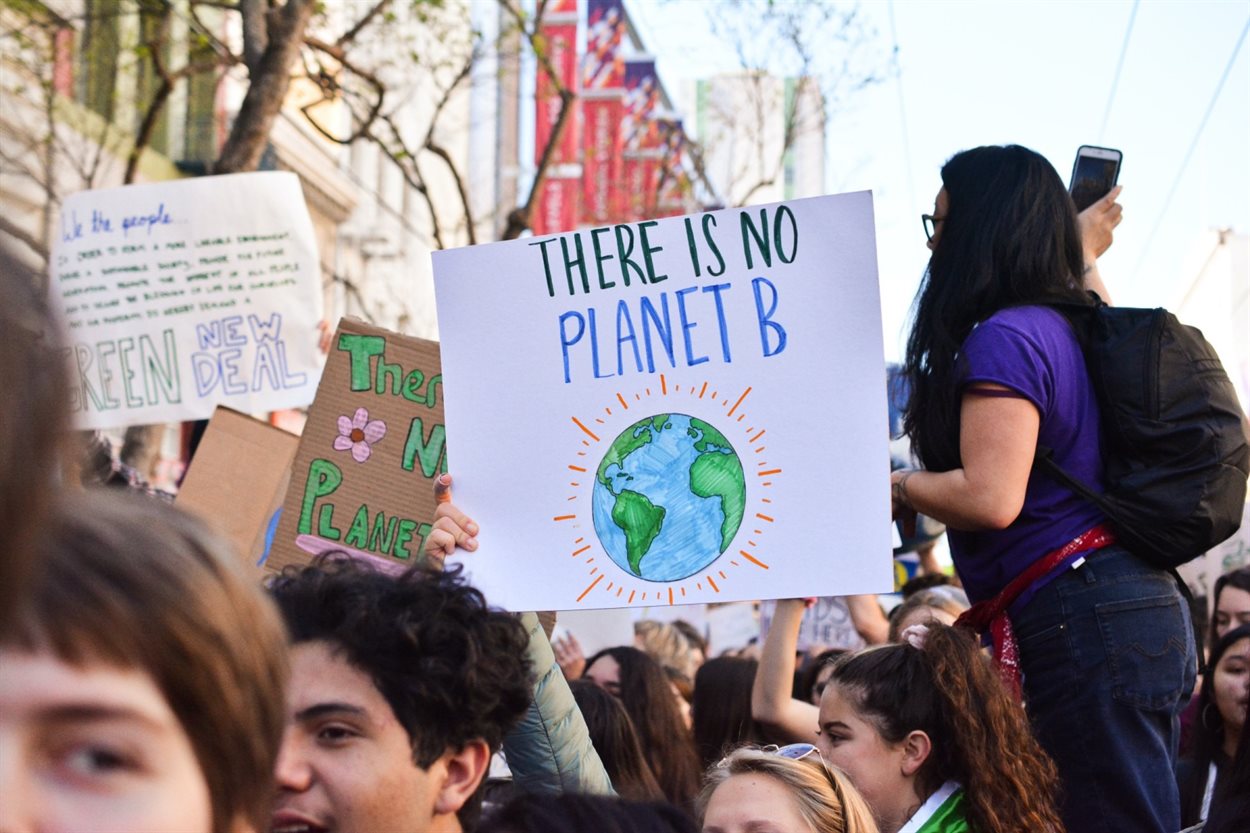 Climate change protestors gather together. One holds a hand-painted sign that says "there is no planet B"