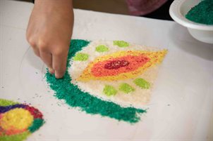Hands creating a rangoli with coloured rice. 