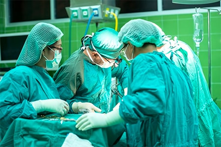 A team of surgeons in medical gowns, caps and gloves performing surgery in theatre