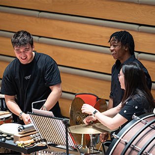 Percussion students stand laughing behind instruments