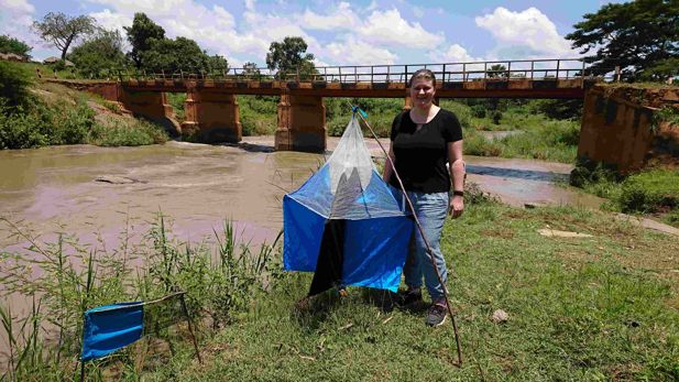 Dr Kat Rock standing by a river near equipment for monitoring insect levels