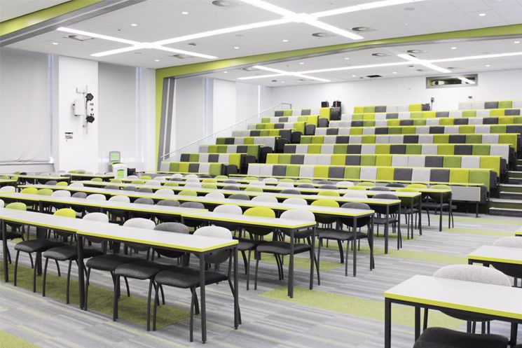 Lecture theatre with green and grey seats and a two rows of grey tables