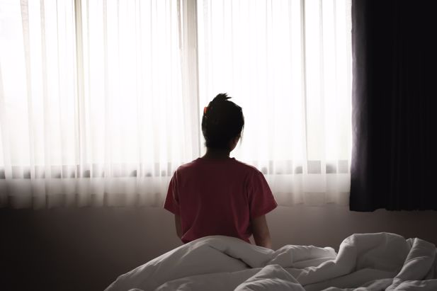 Image of woman sat on bed looking at out a window.
