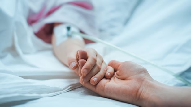 Hand holding a patient's hand in hospital bed.