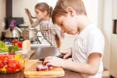 Young child in kitchen chopping vegetables on a wooden chopping board