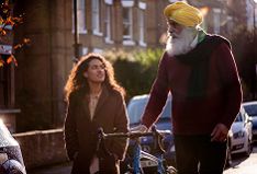 Older Sikh man walking with bicycle and talking with a young woman in the street