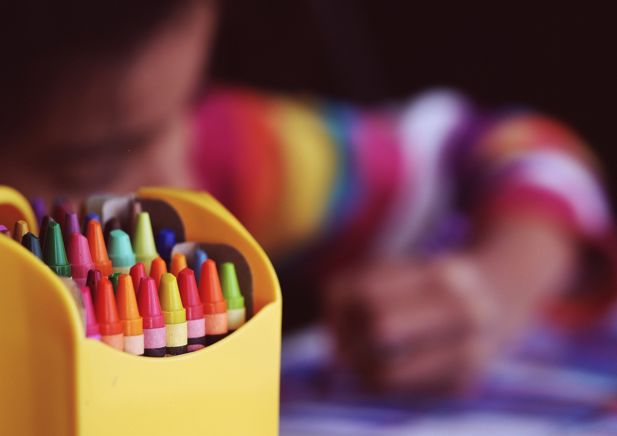 Box of crayons in foreground with blurred child in background colouring