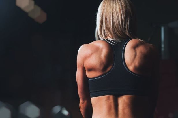 Muscular female athlete in a black sports bra facing away from camera