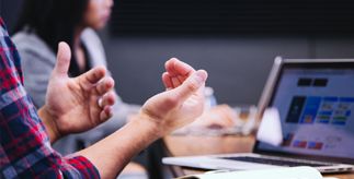 A pair of hands gesturing to colleagues in front of a laptop as people collaborate.