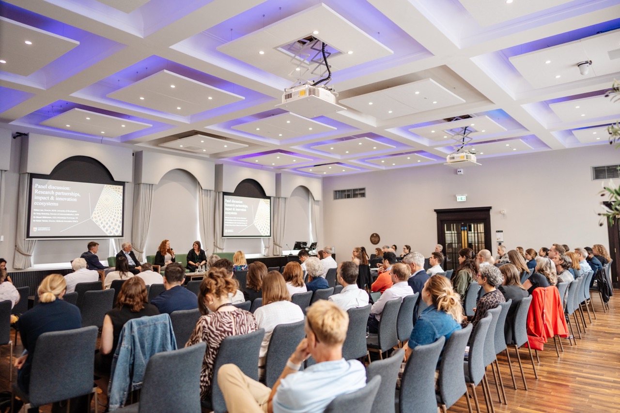 A panel of speakers are sat presenting in front of an audience.