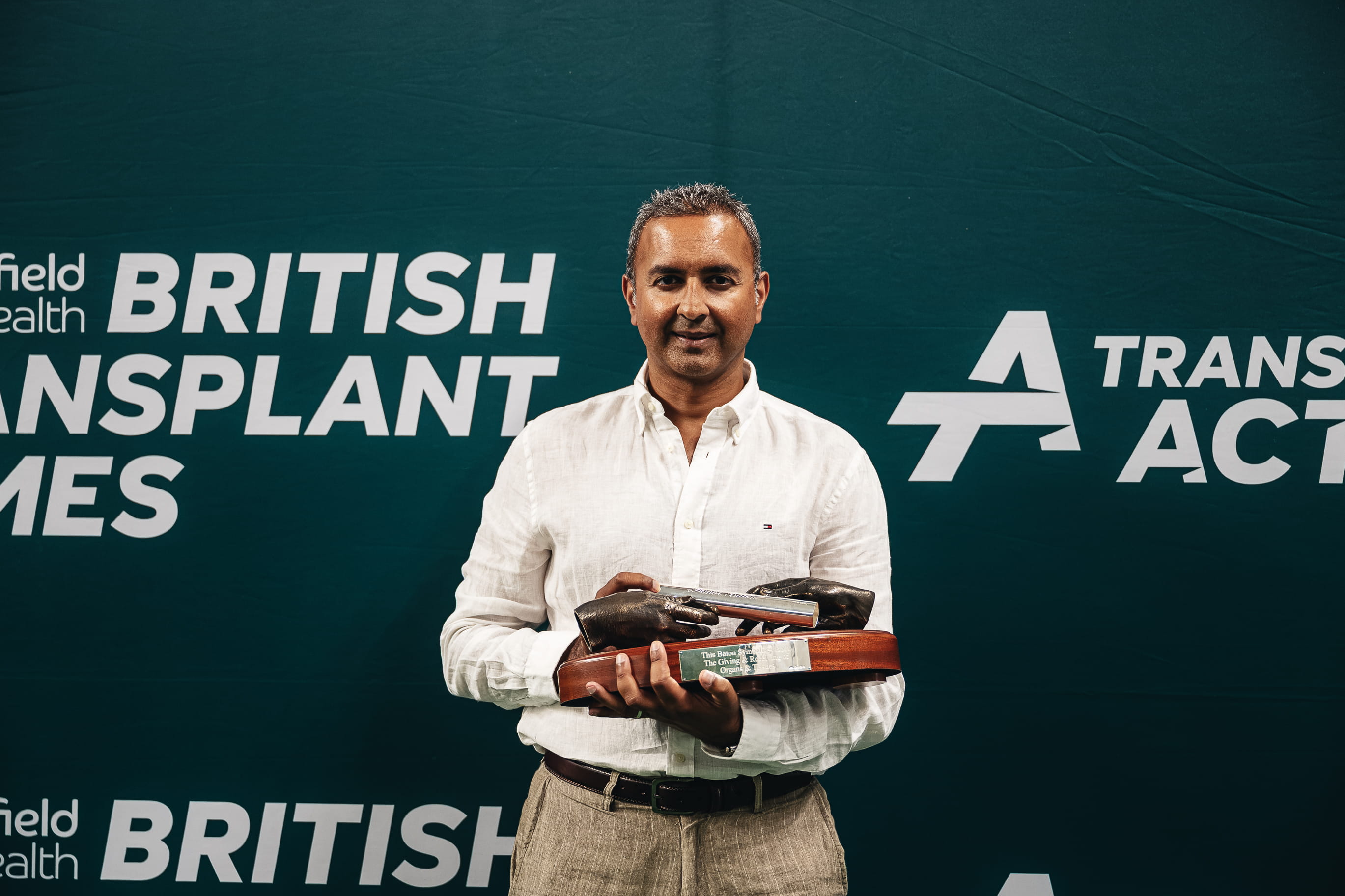 Professor Adnan Sharif holding a baton in front of a backdrop that reads British Transplant Games