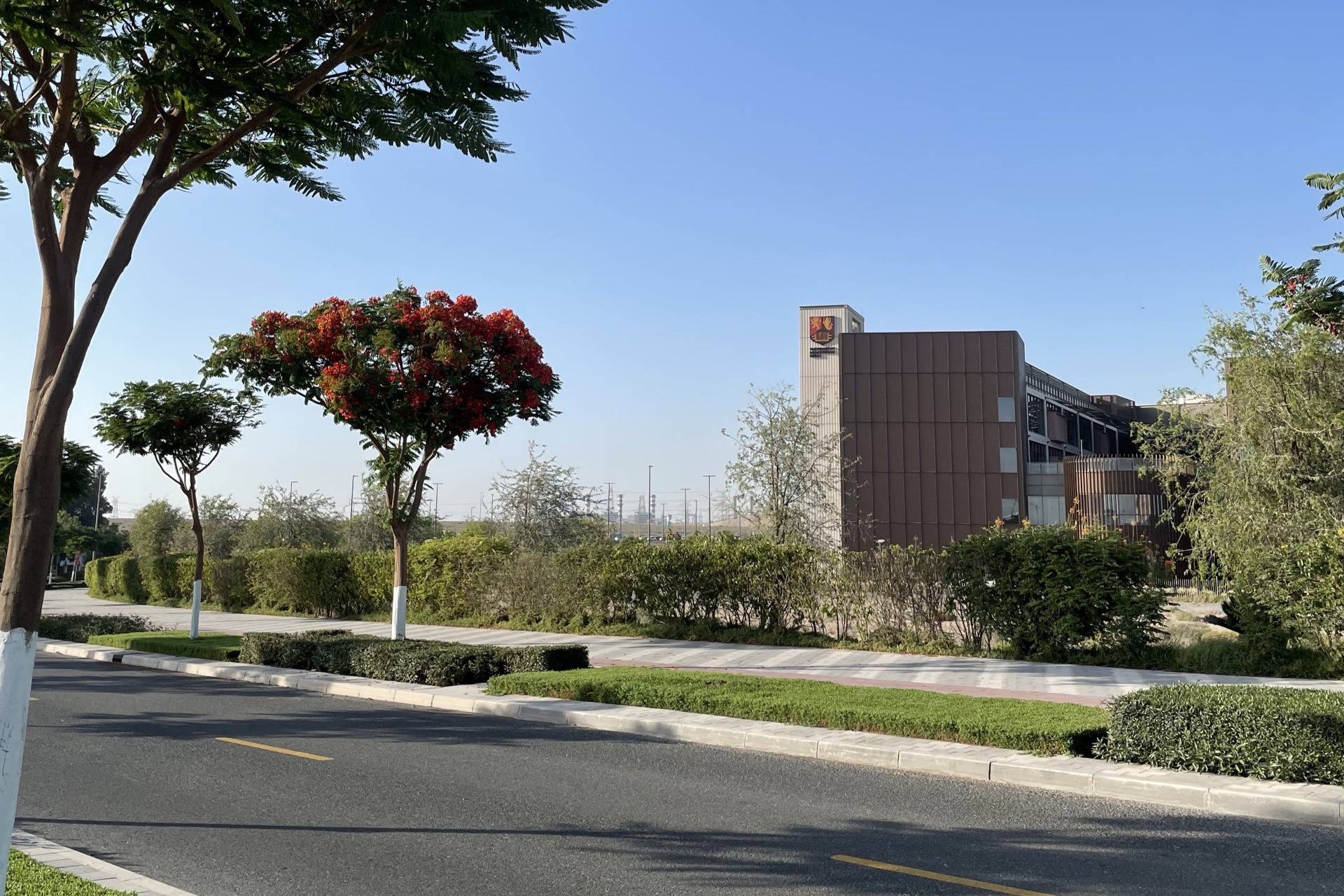 Exterior view of the modern University of Birmingham Dubai campus with greenery in the foreground.