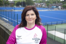 Andrea Edwards, one of the University's Queen's Batonbearers, pictured wearing a Queen's Baton Relay top with University of Birmingham Hockey pitch in background