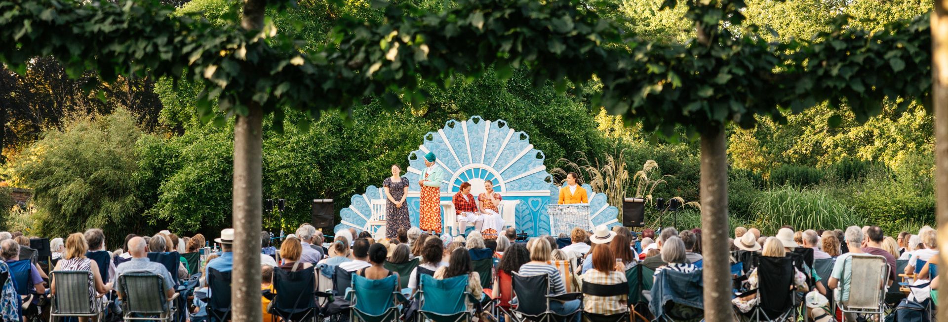 A large crowd sat watching an outdoor theatre performance, with actors wearing period dress