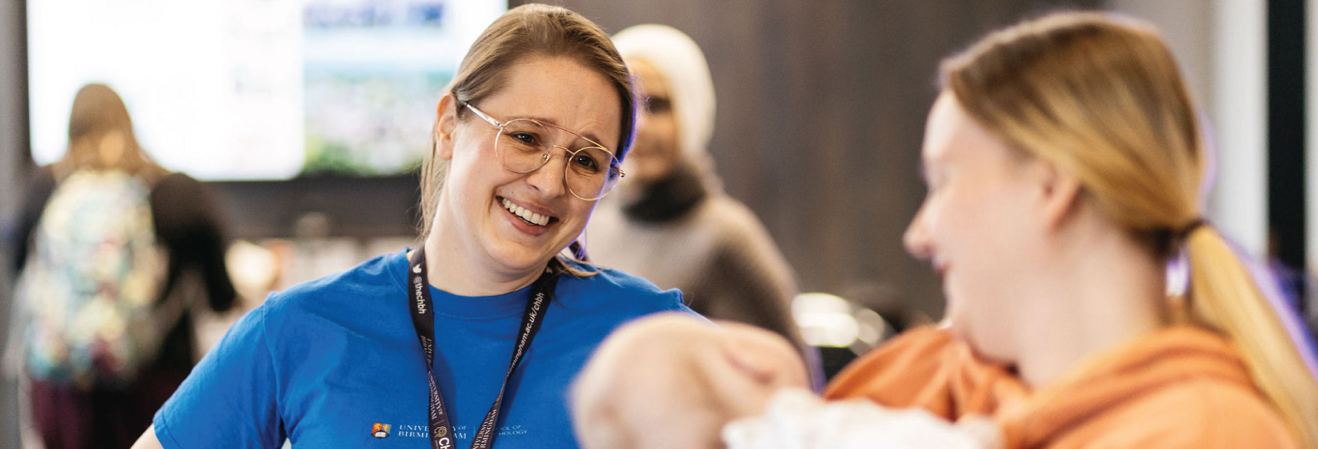 A mother holding her baby talks to a member of BabyLab staff in a blue t-shirt.