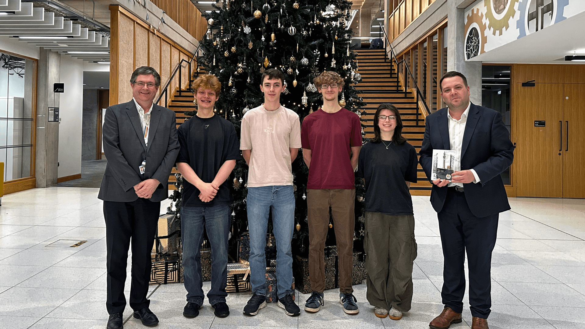 four winners standing with Professor Andrew Quinn and Professor Matt Leeke in front of a Christmas tree