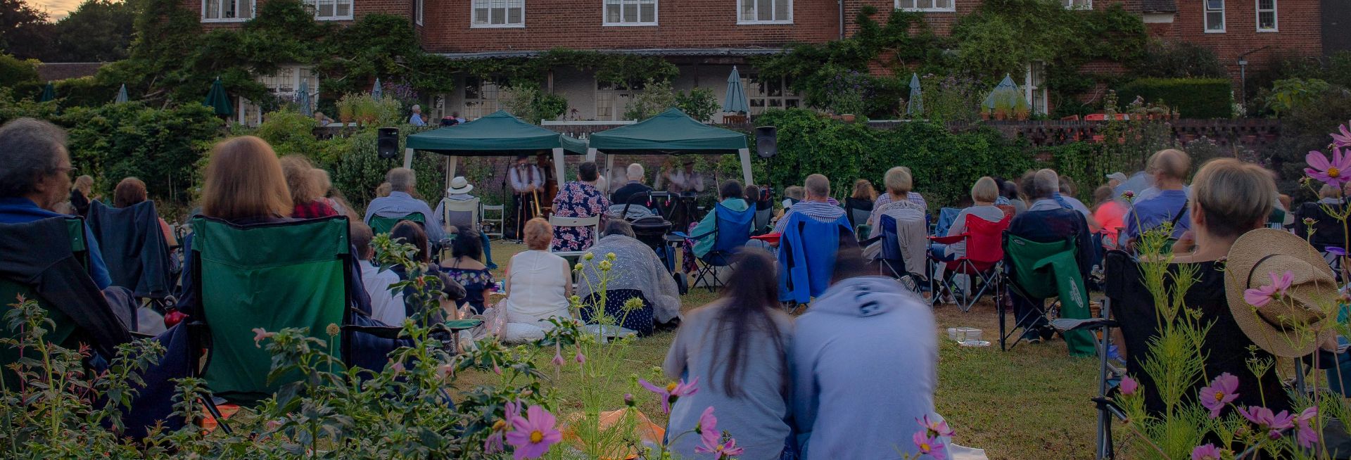 People sat on a lawn watching musicians performing under a gazebo