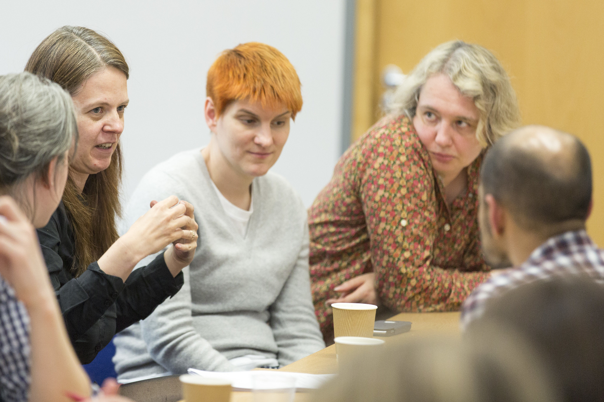 A woman gesticulating with hands to a group of other women around a table.