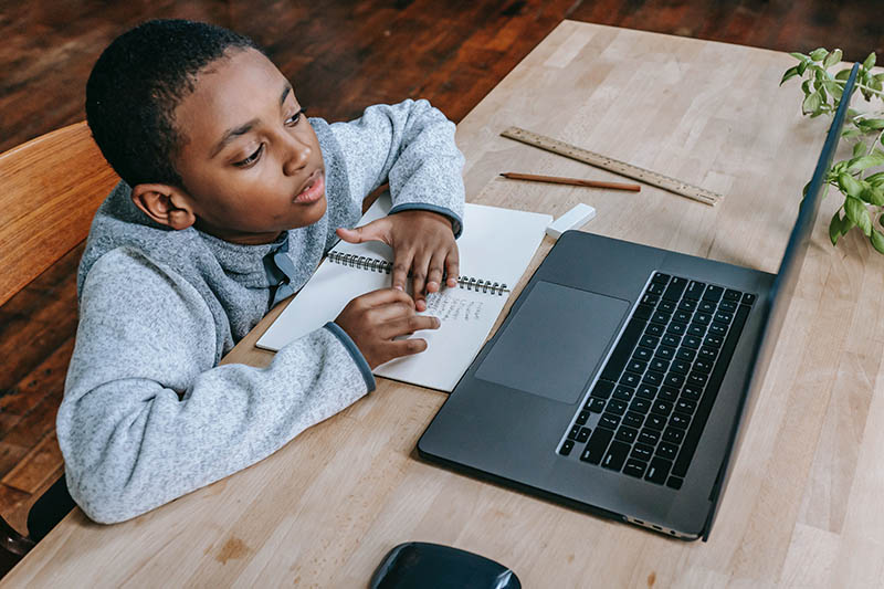 Young boy working in front of laptop with notepad in front of him