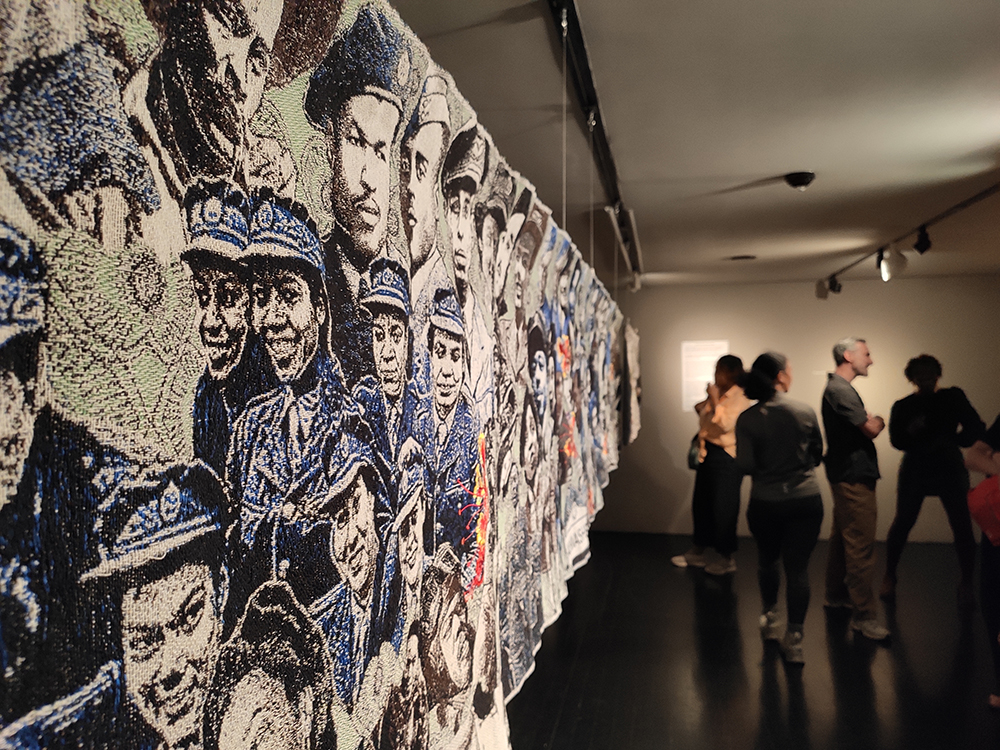 A tapestry full of faces displayed at a museum gallery