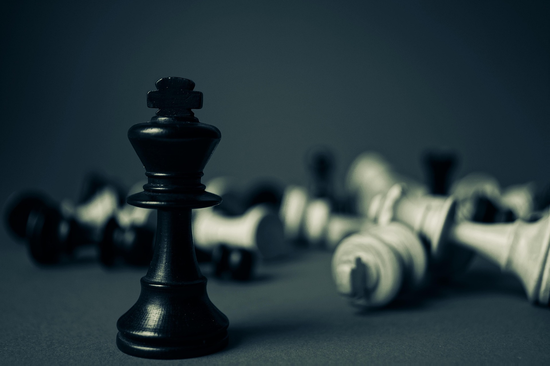 A black chess piece remains standing amonst fallen white pieces