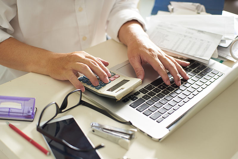 man working on a laptop and also using a calculator