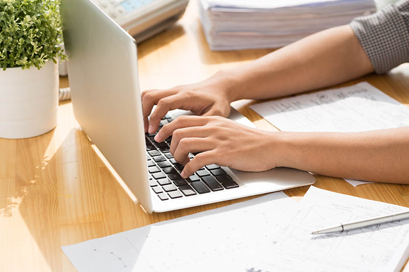 A person typing on a laptop which is on a desk 