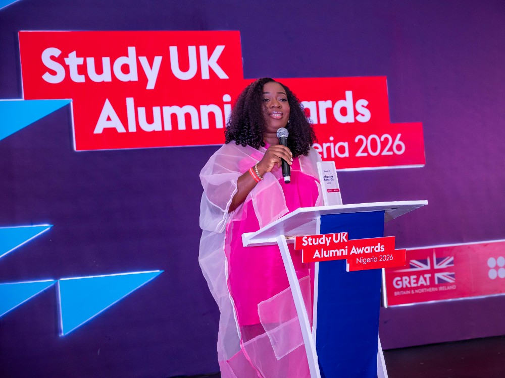 Study UK winner Yemisi Odusanya on a stage with a microphone. Behind her is the red and white Study UK logo
