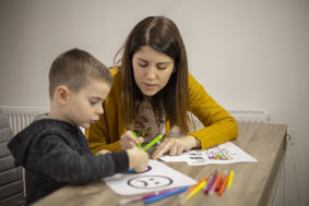 A woman assisting a young boy with his drawing