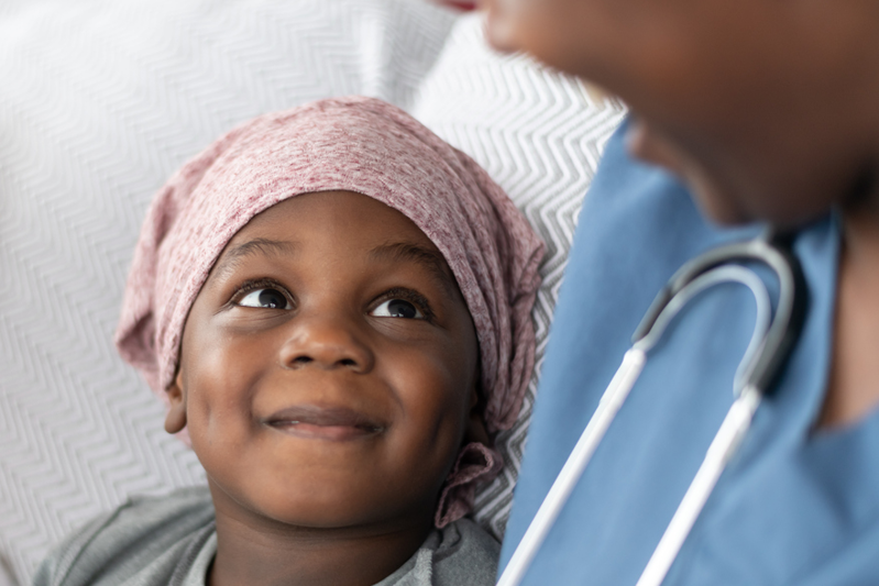 Young child wearing head scarf covering hair loss smiling up at nurse