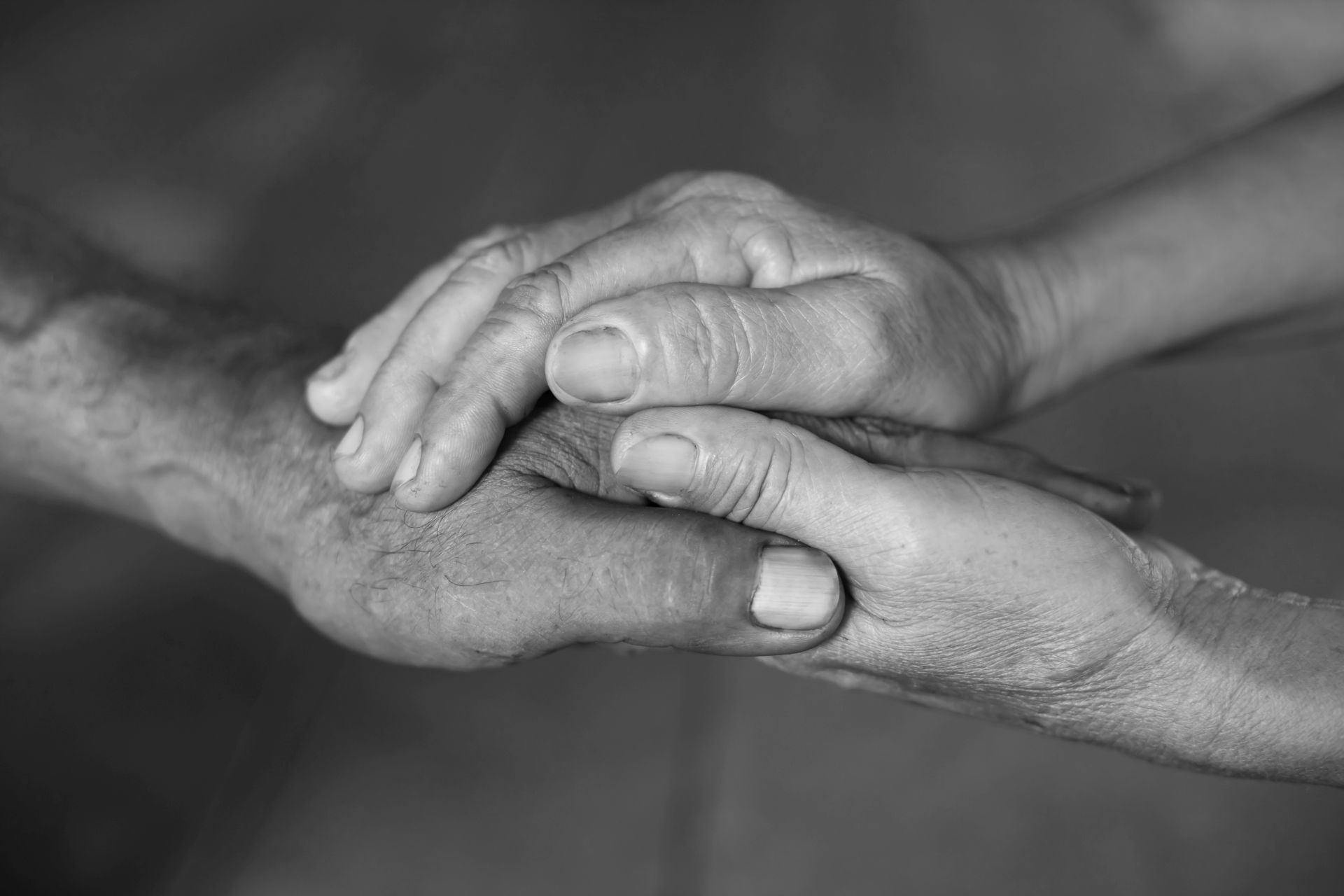 Monochrome image of the hands of an elderly woman holding the hand of an elderly man