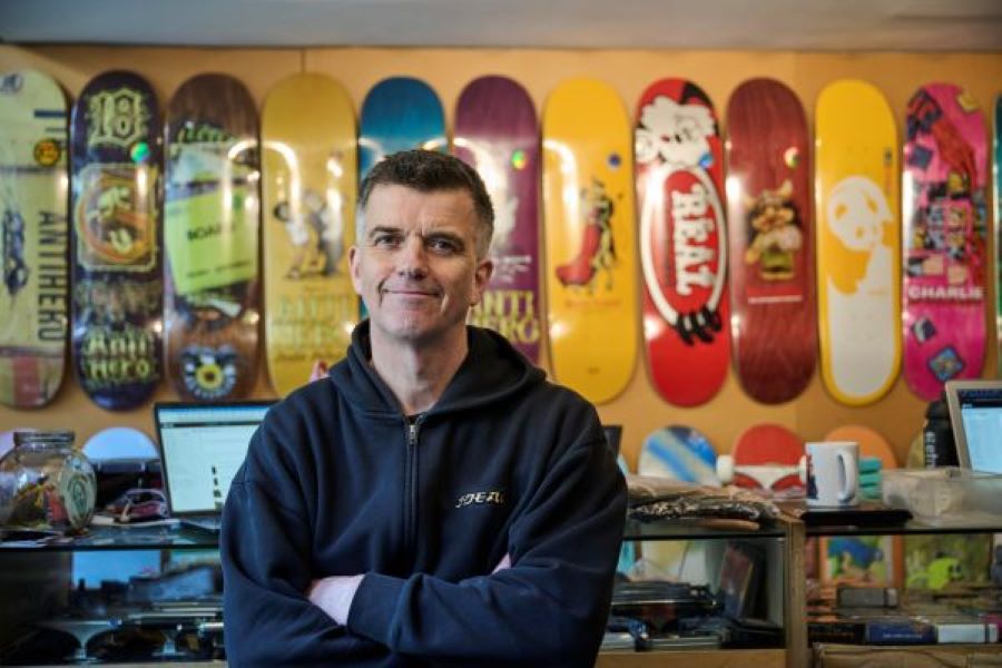 Man smiling with arms crossed in a skateboard shop with skateboards on the wall