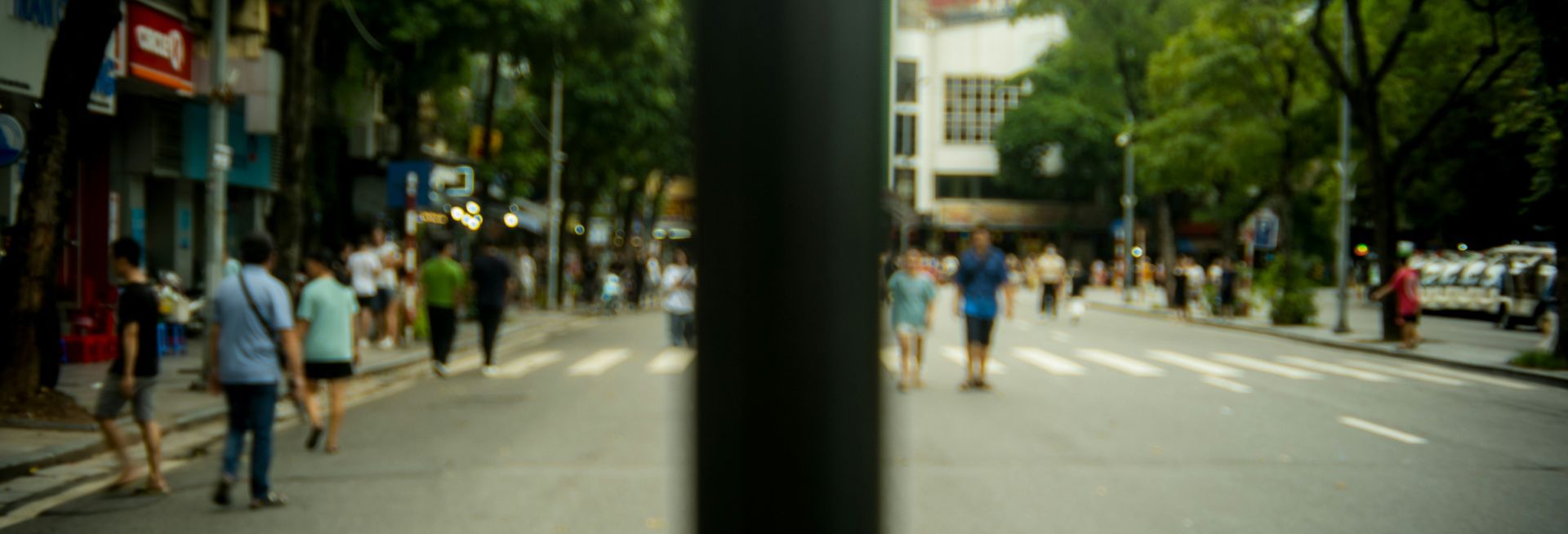 A blurry street scene with people walking in the road. A pole obstructs the view in the middle