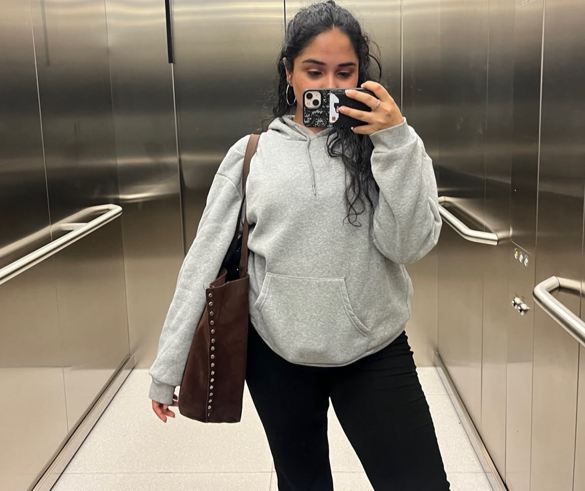 Diya wearing a grey hoodie smiling in a lift mirror