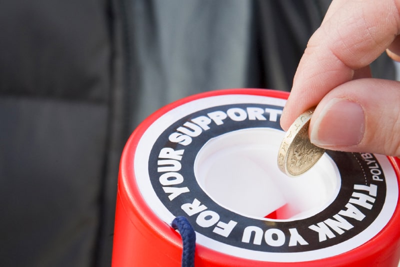 A hand putting a one pound coin into a charity collection box