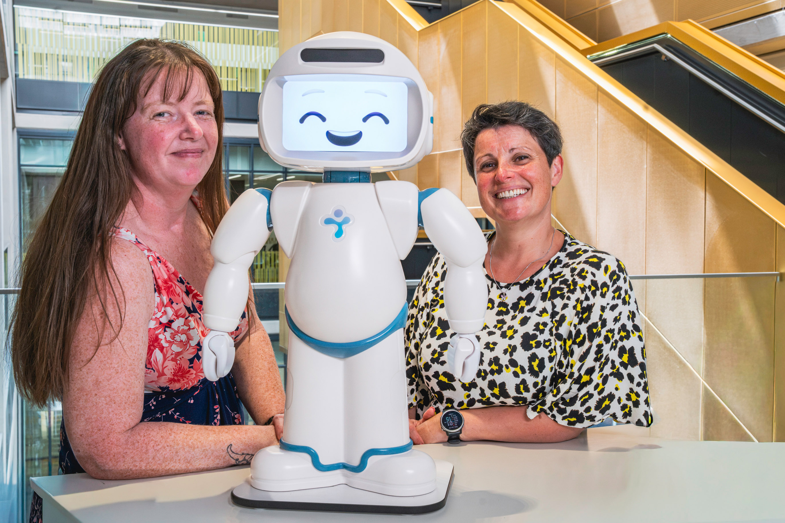 Two women pose alongside a child-friendly robot