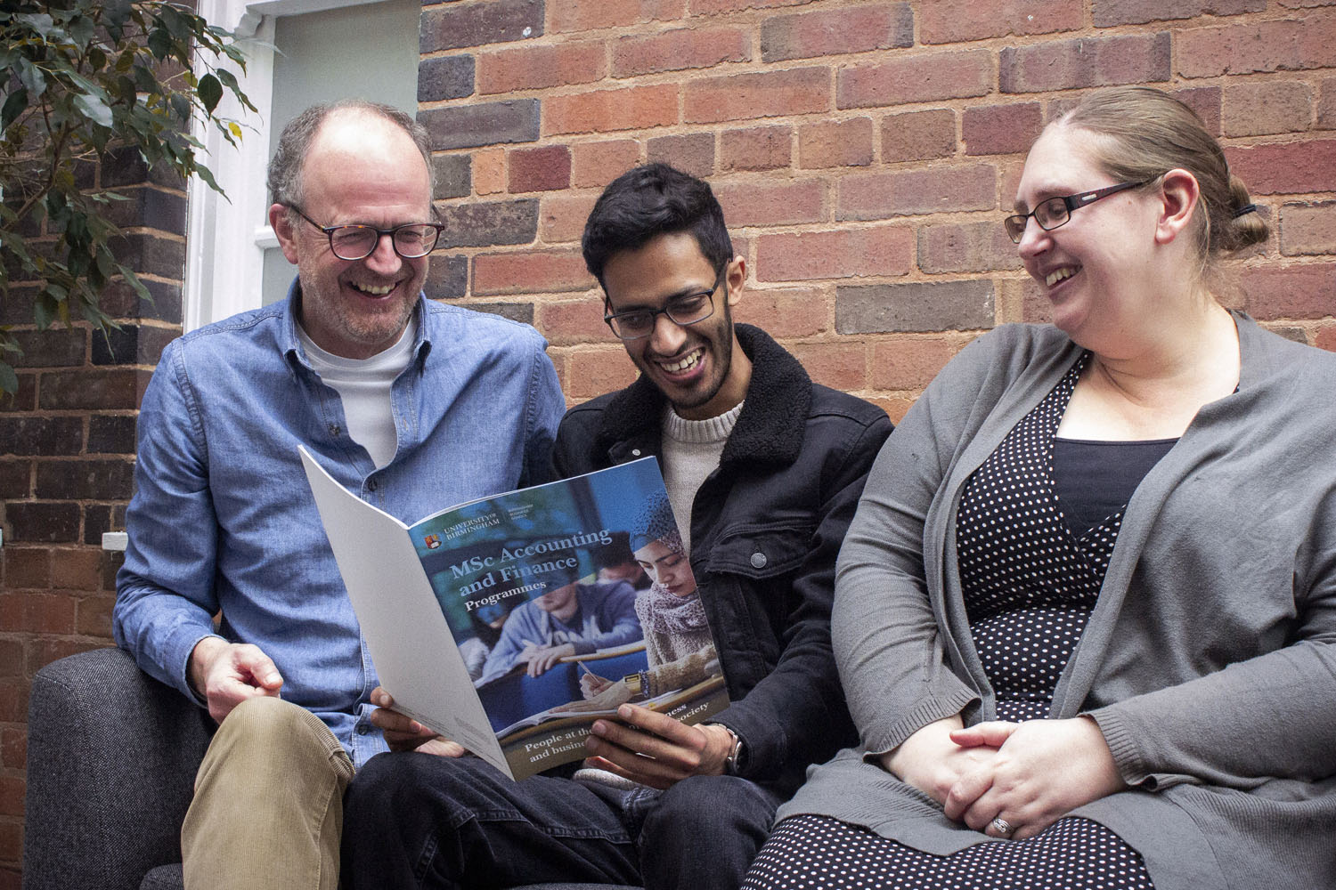 A man sits and reads a prospectus with his parents either side of him
